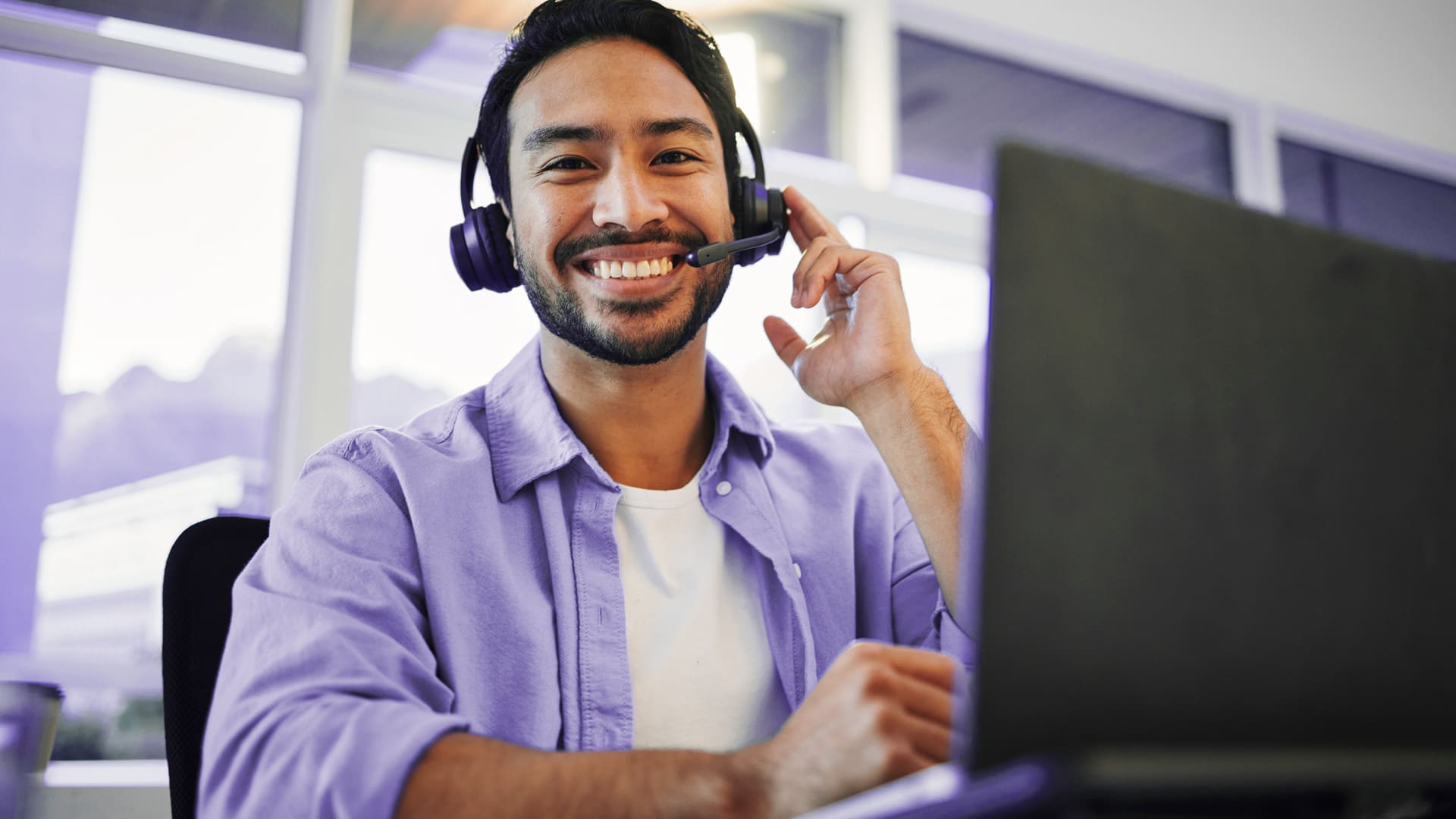 Hombre sonriente con camiseta lila trabajando como agente en un contact center