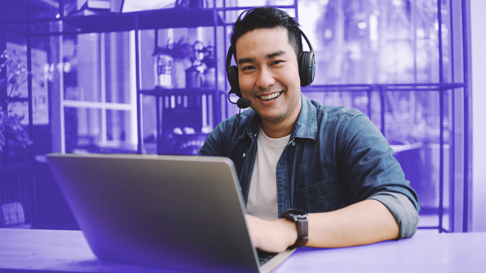 Hombre asiático sonriendo a la cámara mientras trabaja en un call center con su portátil y auriculares