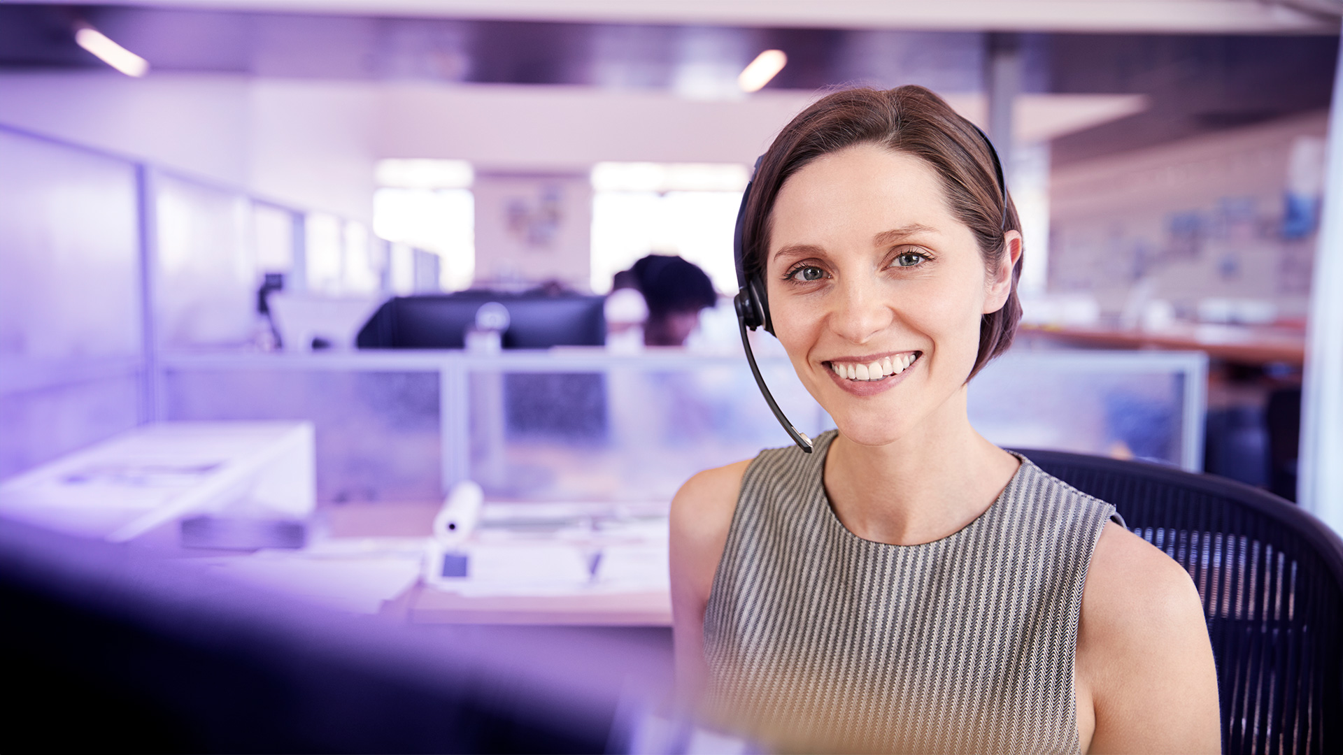 Mujer sonriendo a cámara mientras trabaja en un call center