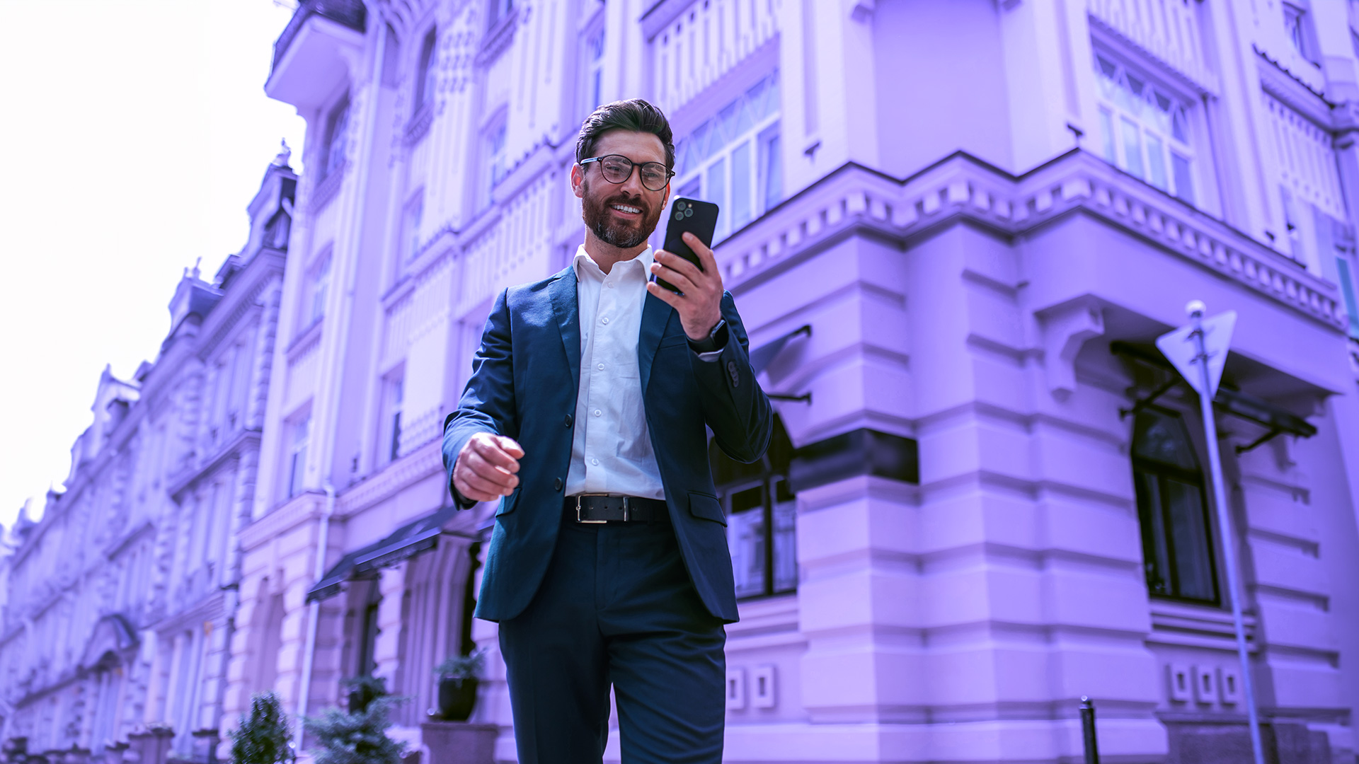 Hombre trajeado delante de un juzgado sosteniendo su teléfono móvil mientras chatea con su bufete de abogados