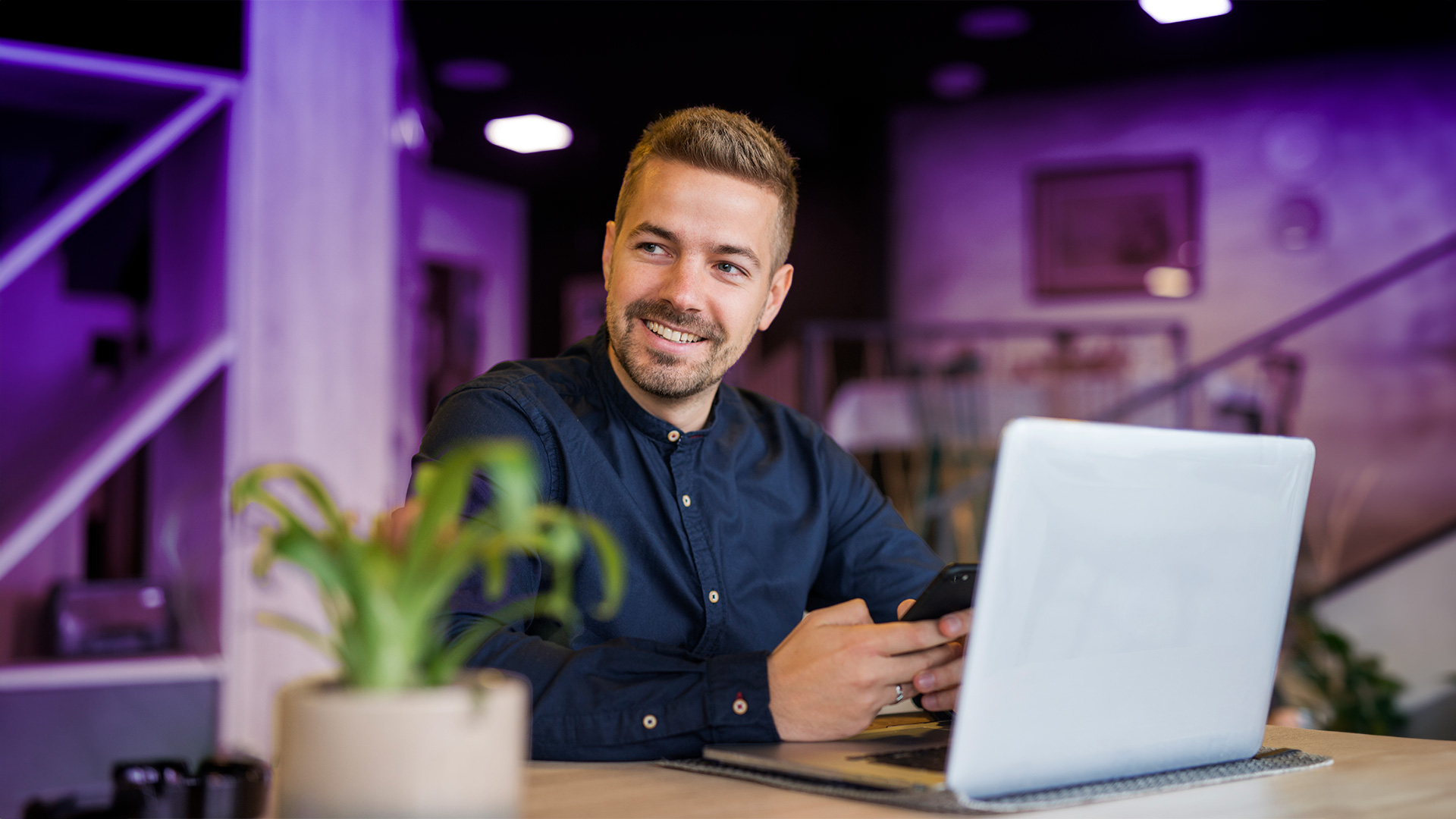Hombre joven y sonriente que trabaja como director de recursos humanos con el móvil de su trabajo en las manos escribiendo une mail mientras lee el resumen de la transcripción de una reunión que ha redactado Shomi, el asistente personal de Enreach Contact