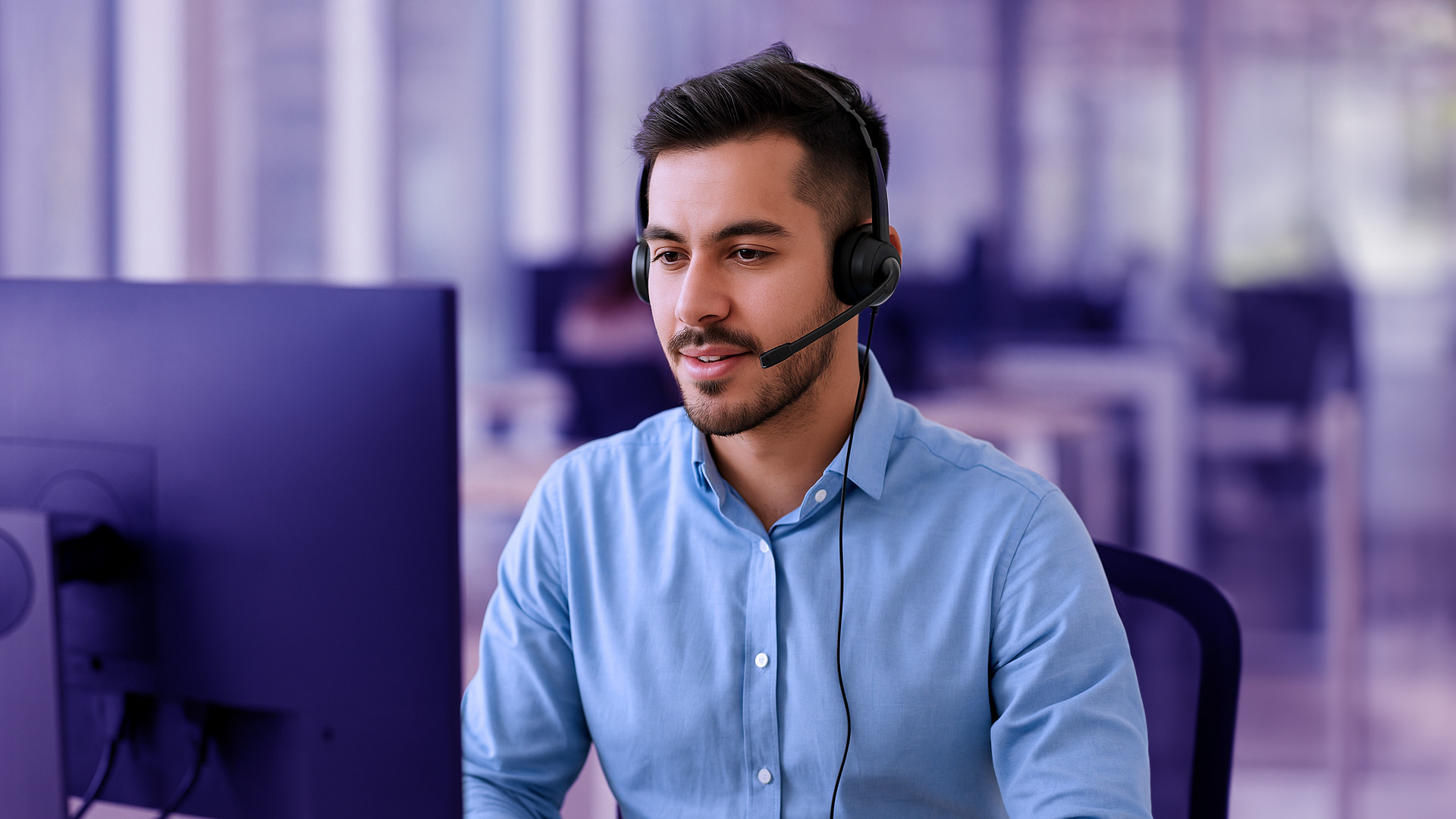 Hombre agente de contact center mirando su pantalla de ordenador con expresión de concentración